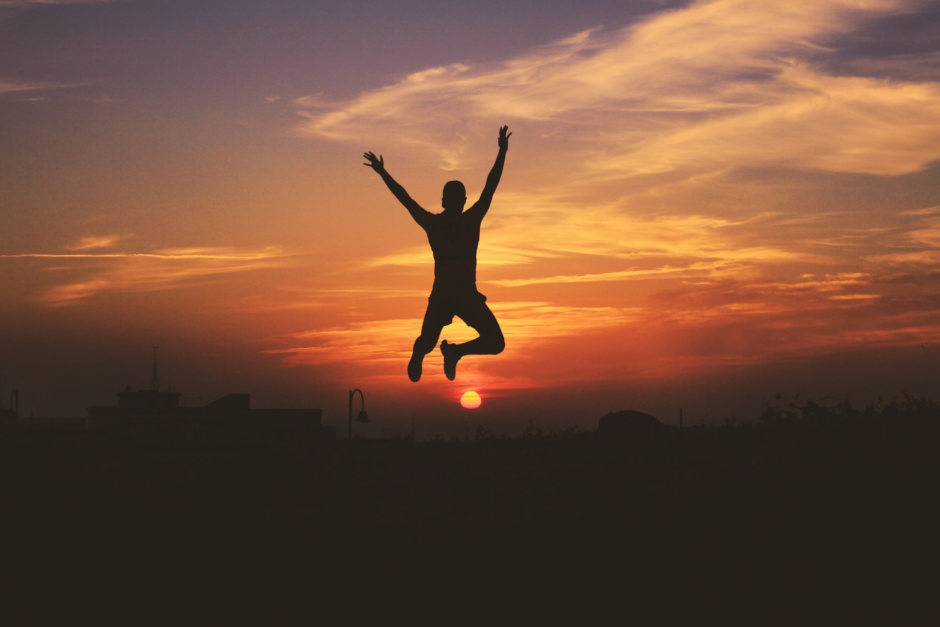 silhouette of man jumping raising both hands during golden hour